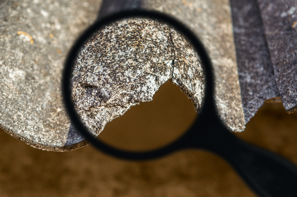 Una lente di ingrandimento che punta sul bordo rovinato di una lastra di amianto